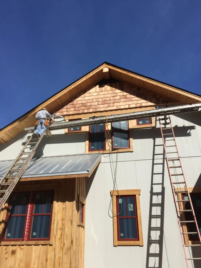 New gable with cedar shingle accents and a metal roof over a window, with a worker on a ladder
