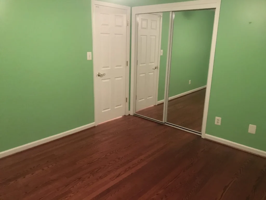 Bedroom with green walls, mirrored closet doors and hardwood floor