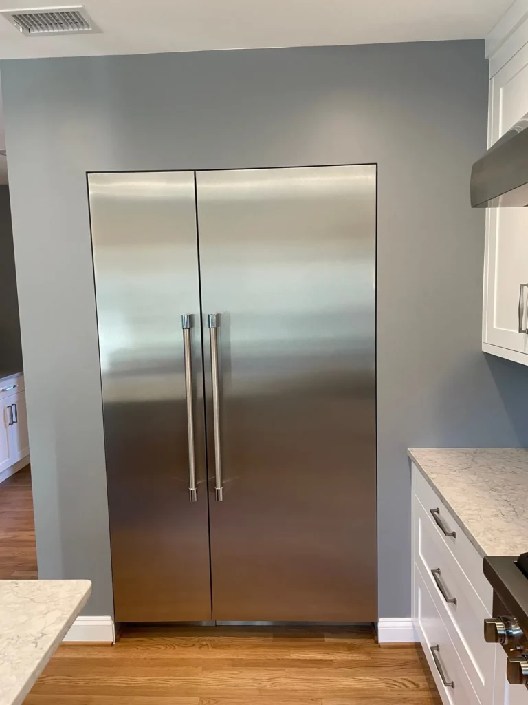 Stainless built-in refrigerator set between white cabinets