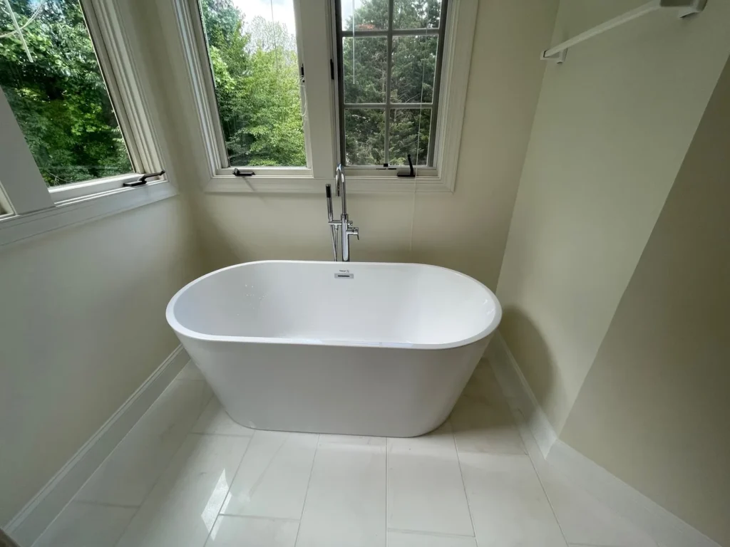 White freestanding tub with a floor-mounted faucet under casement windows