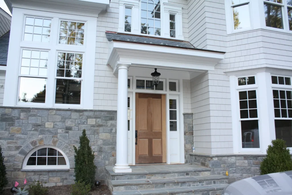 Front entry with a covered portico, stone base and white shingle siding