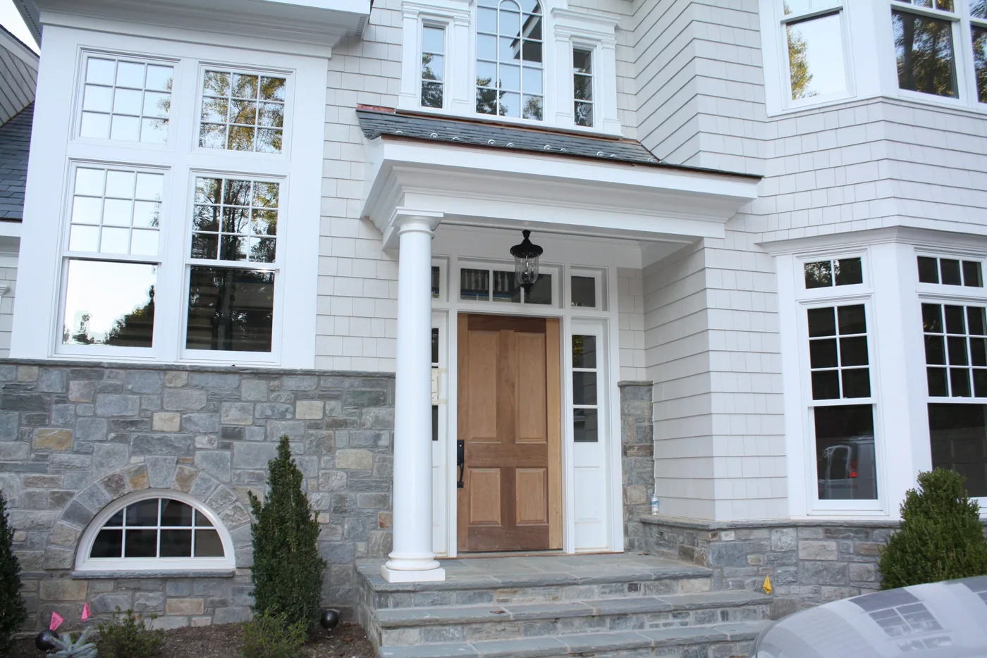 Front entry with a covered portico, stone base and white shingle siding
