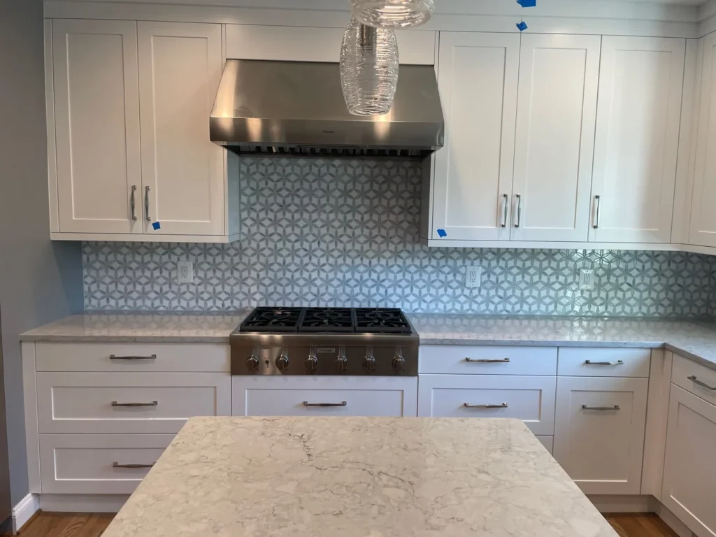 White cabinets around a stainless range hood with a gray hexagon tile backsplash