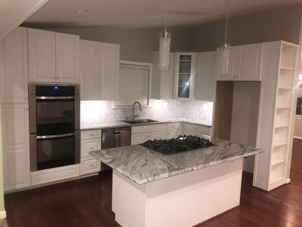 Kitchen island with a gas cooktop beside double wall ovens and white cabinets