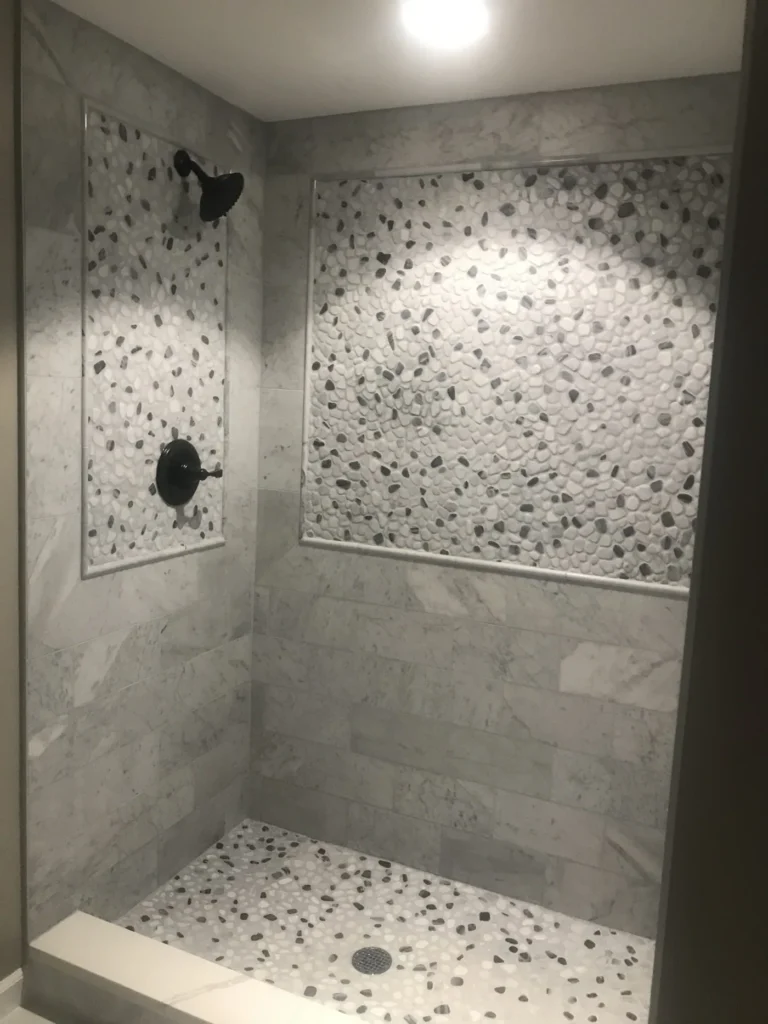 Custom walk-in shower with marble-look tile and a pebble mosaic accent