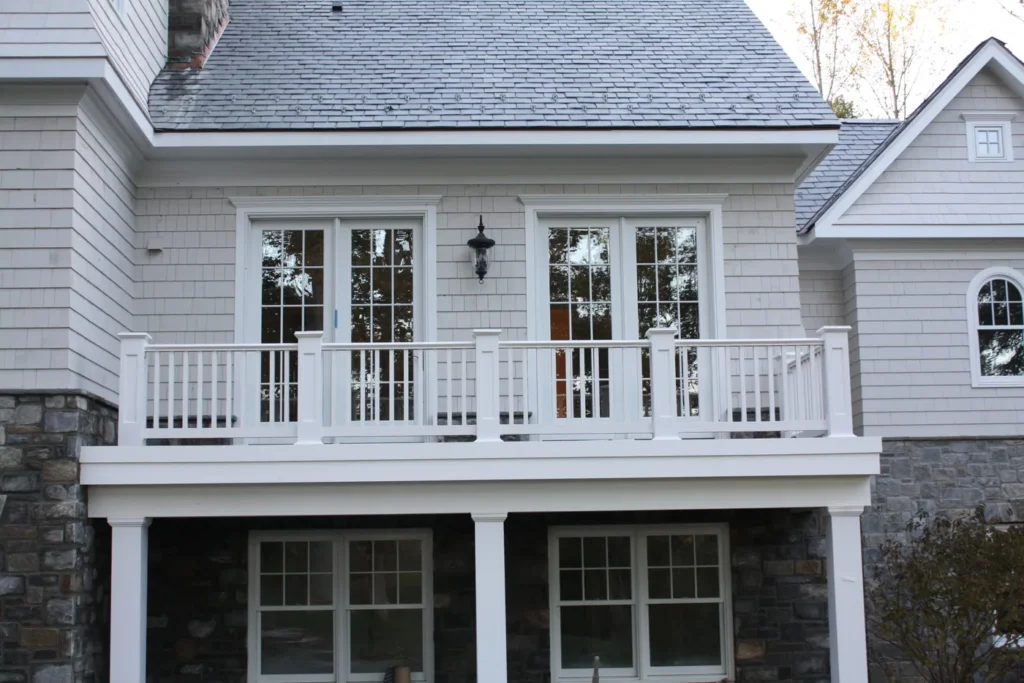 One of our home additions: rear addition with a stone base, French doors and a white railed balcony