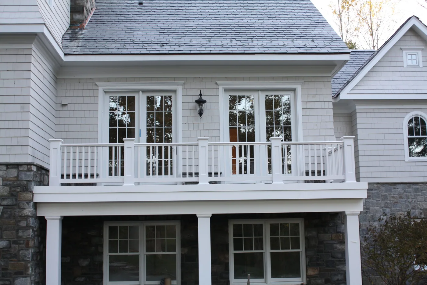 One of our home additions: rear addition with a stone base, French doors and a white railed balcony