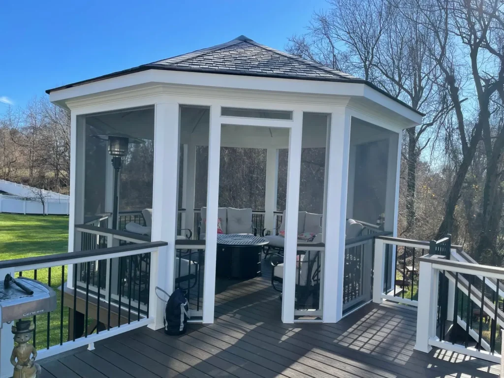 White screened octagonal gazebo with a shingle roof and black railings under a blue sky