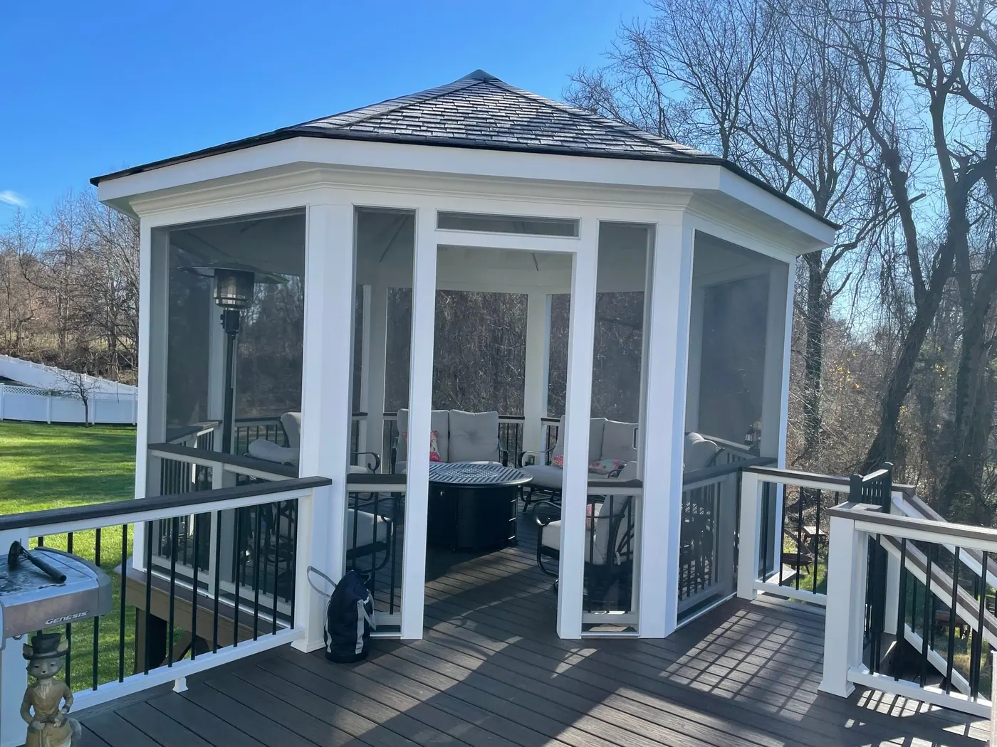 White screened octagonal gazebo with a shingle roof and black railings under a blue sky