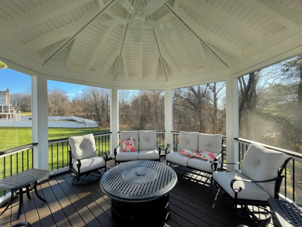Inside a screened porch with a white vaulted ceiling, patio furniture and a fire table