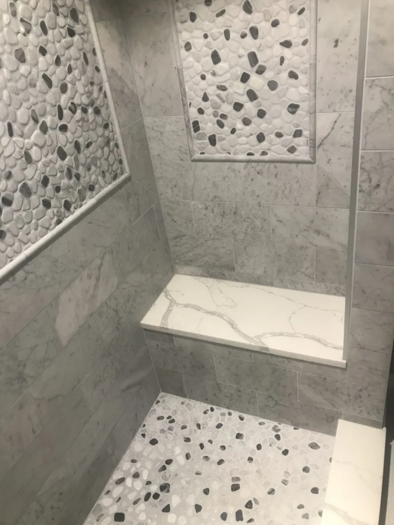 Tiled shower with a corner bench and a pebble mosaic panel