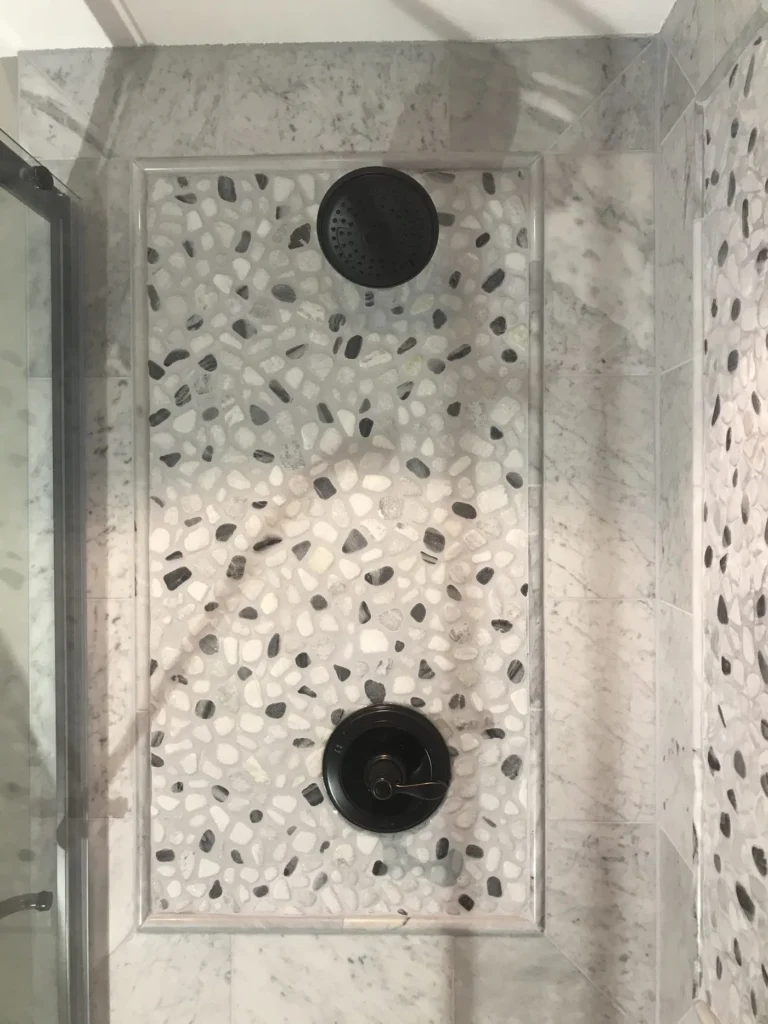 Shower wall with a pebble mosaic panel and black fixtures