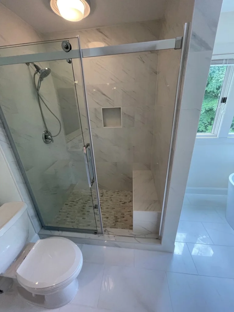 Walk-in shower with a sliding glass door, a tiled niche and a pebble floor