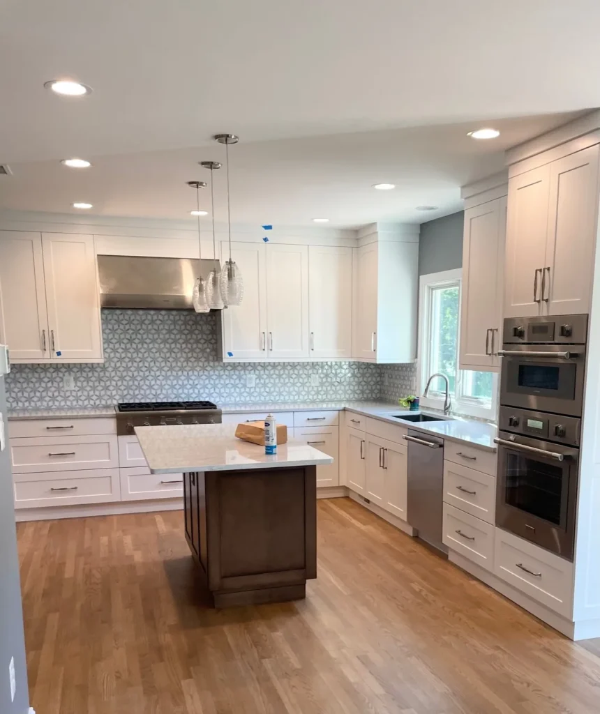 White shaker kitchen with double wall ovens, an island and recessed lights