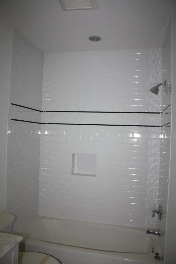 Tub and shower in white tile with a thin dark accent stripe